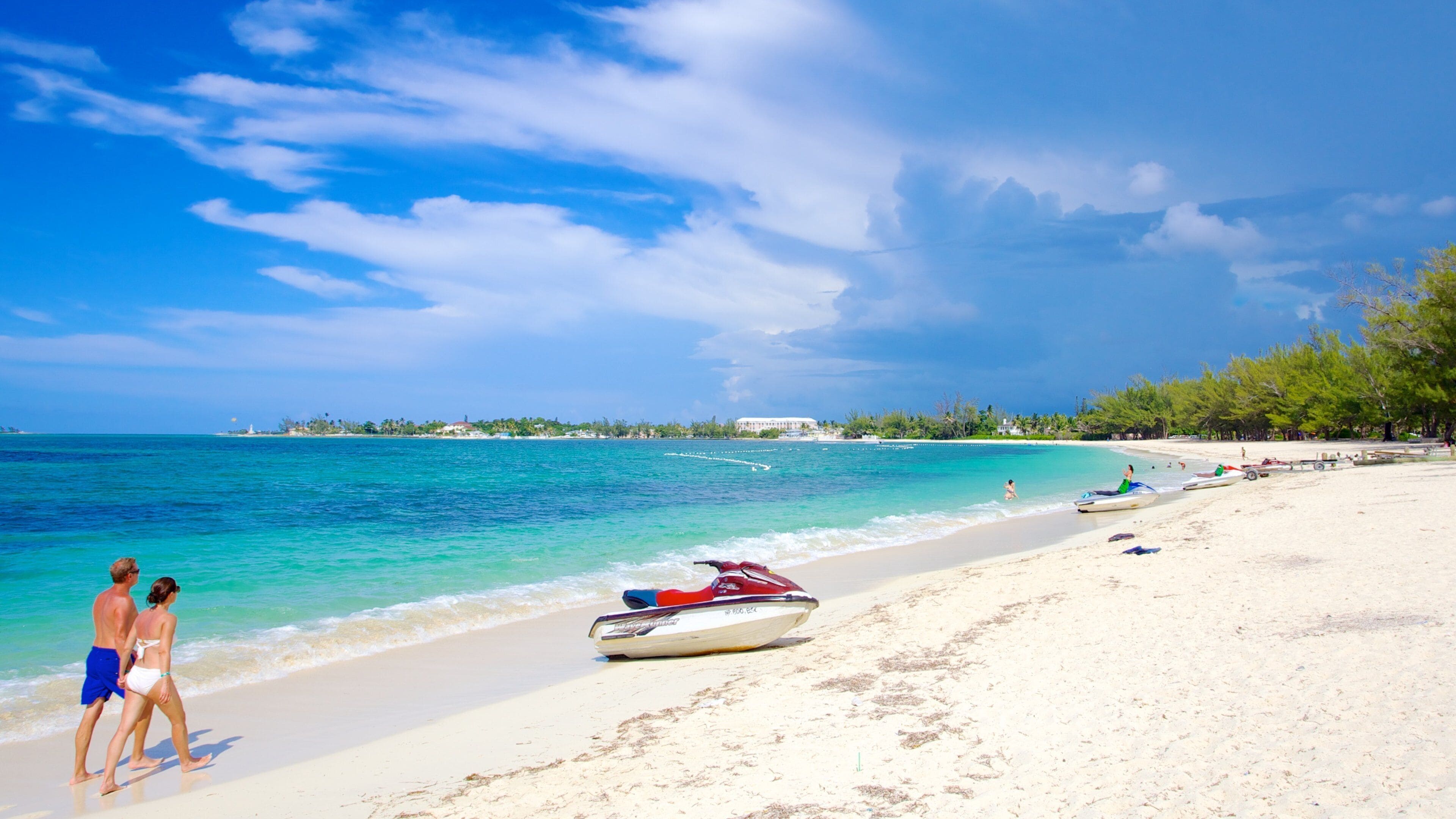 Couple walking a Nassau shoreline beside a beached jet ski: the time and lifestyle Cable Bahamas employees get back when payroll runs in a day and a half.