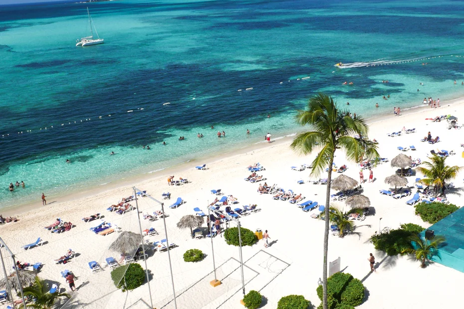 Nassau resort beach with catamaran and sunbathers: the Bahamian economy Cable Bahamas connects through broadband and mobile.